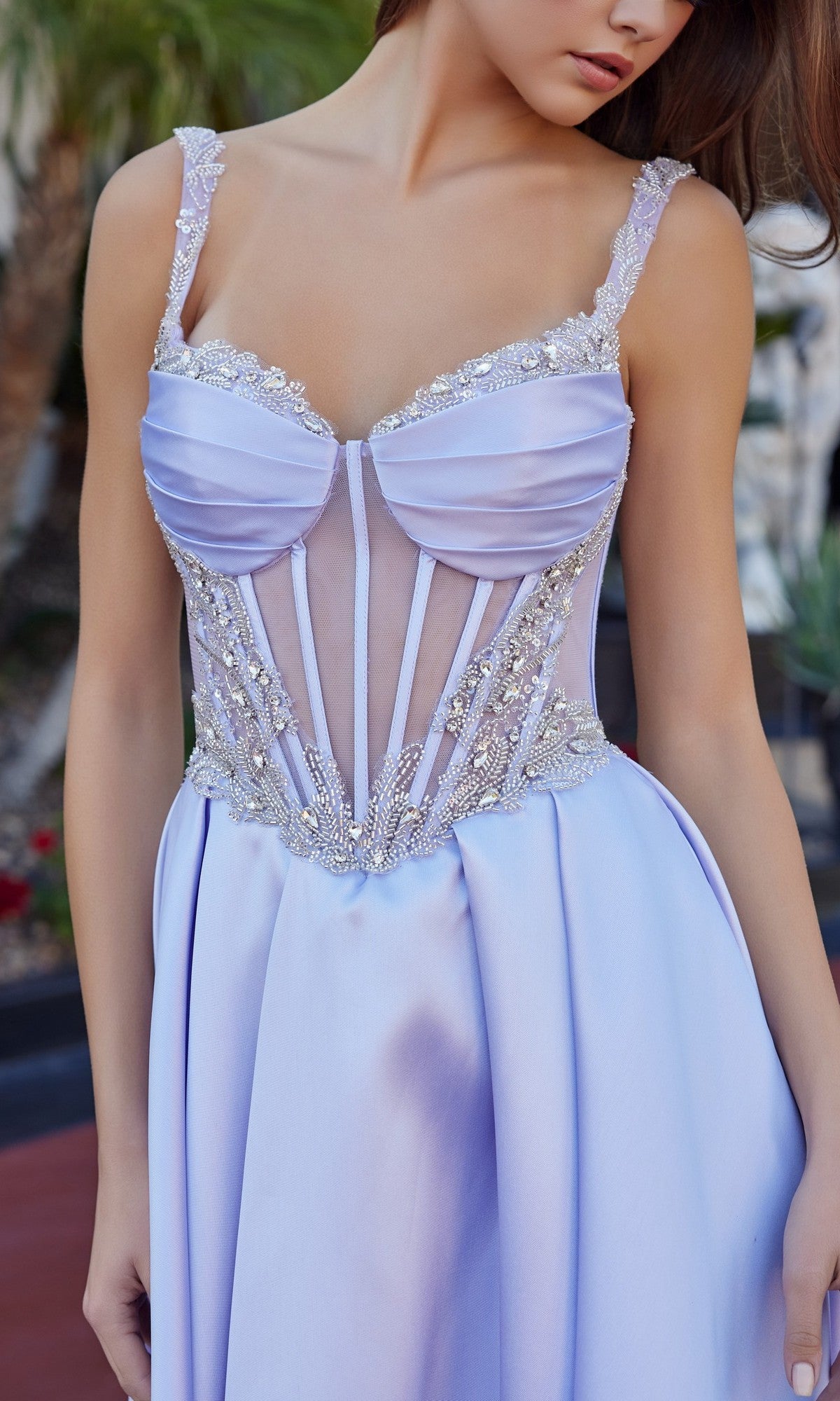 A woman wearing the Nox Anabel Q1775 Long Prom Dress in light purple satin, featuring a floor-length skirt, sheer corset bodice with beaded details, spaghetti straps, and a high-leg slit.